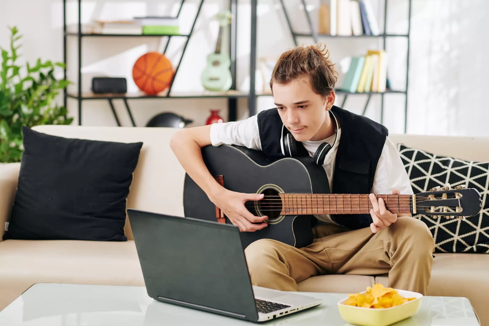 adolescente aprende a tocar la guitarra sentado frente a portatil