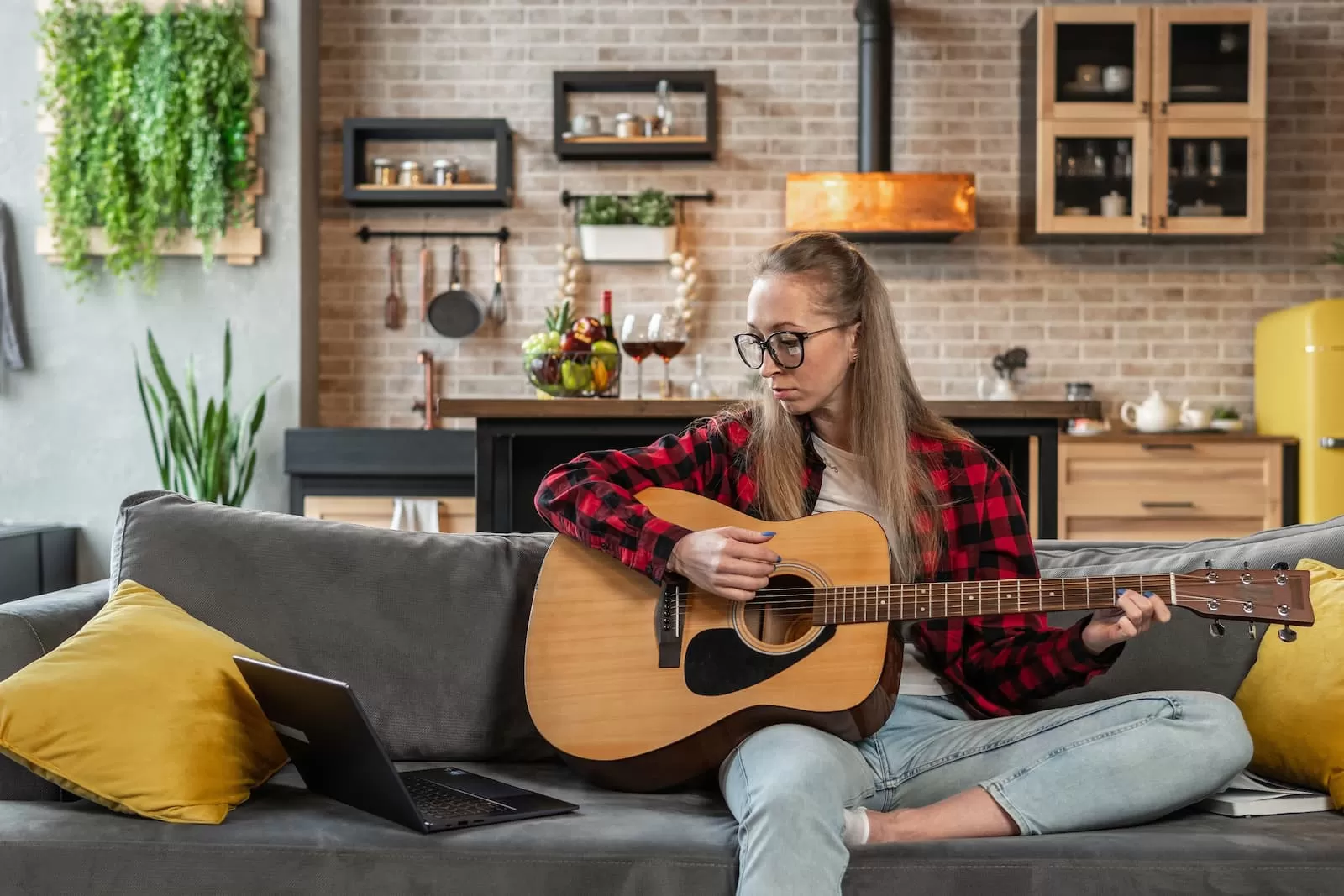 chica adolescente rubia en el sofa aprende a tocar la guitarra mirando la tablet