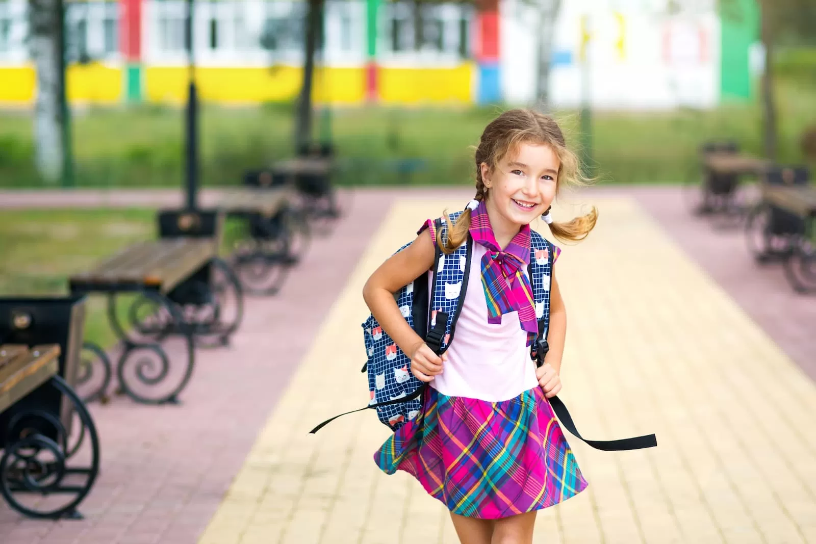 chica alegre con mochila y uniforme escolar en el patio de la escuela