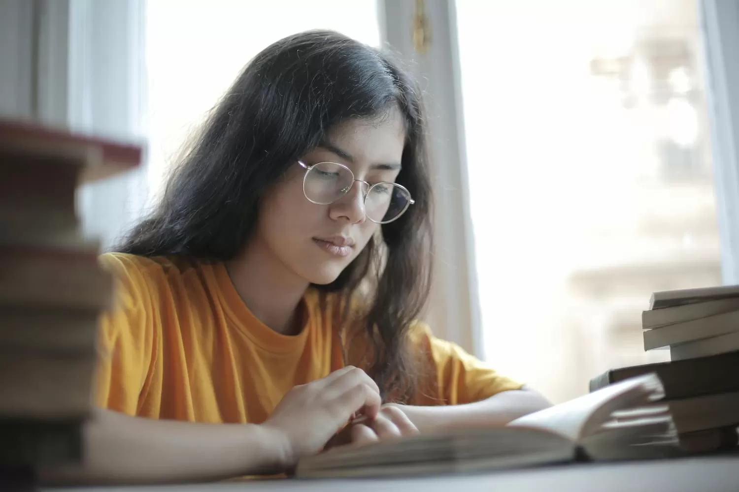 chica estudia para selectividad sentada frente a una mesa llena de libros