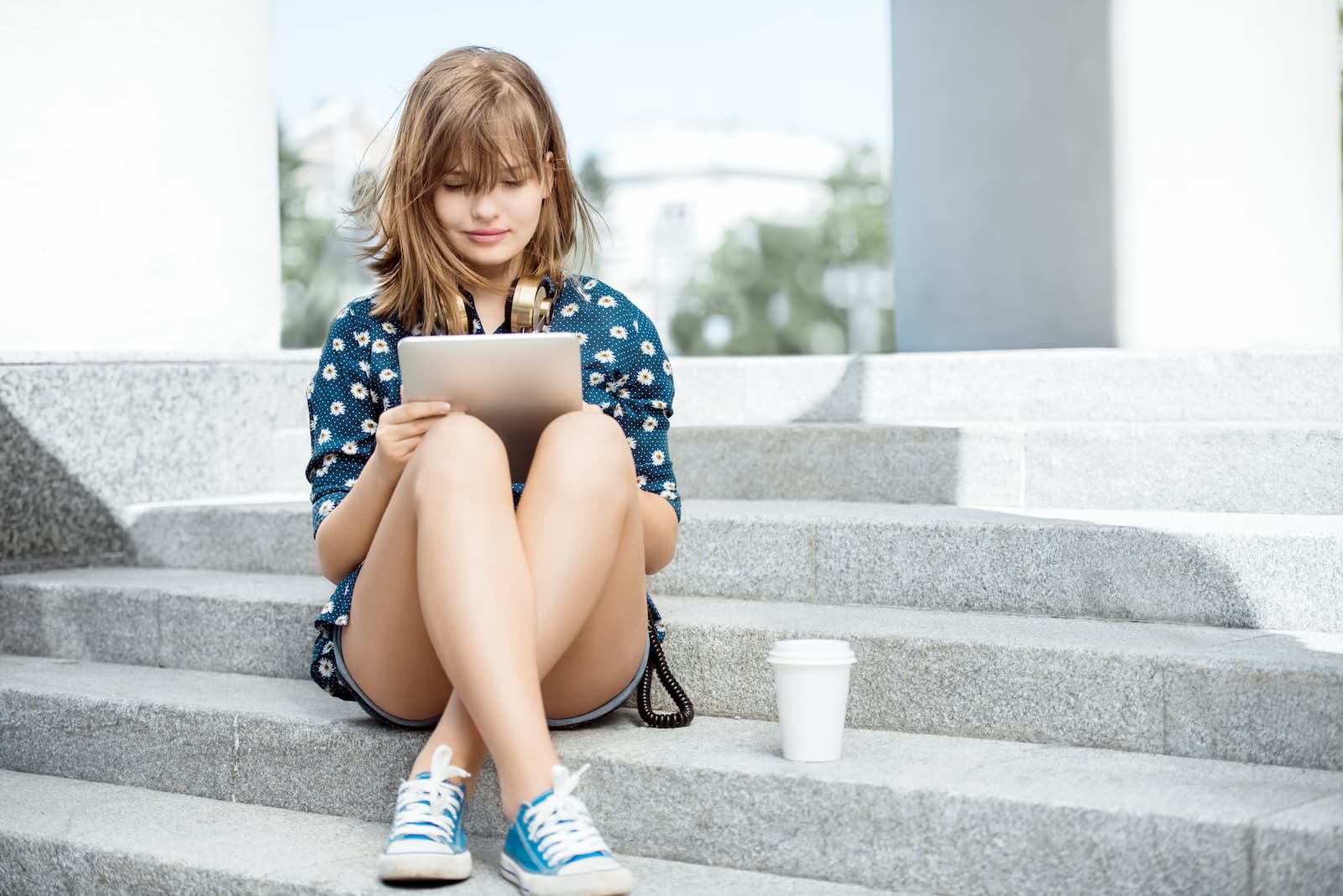 chica rubia joven sentada en escalera leyendo en una tablet