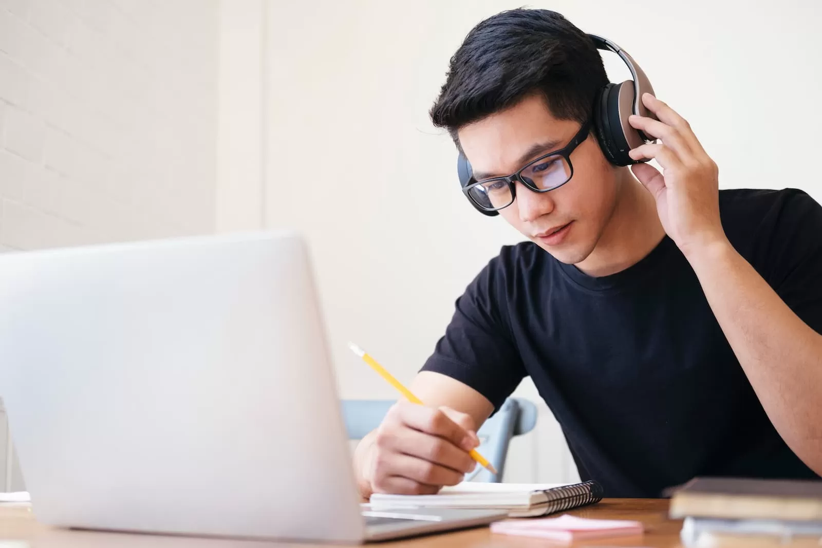 chico moreno joven con cascos frente a un portatil blanco estudiando online