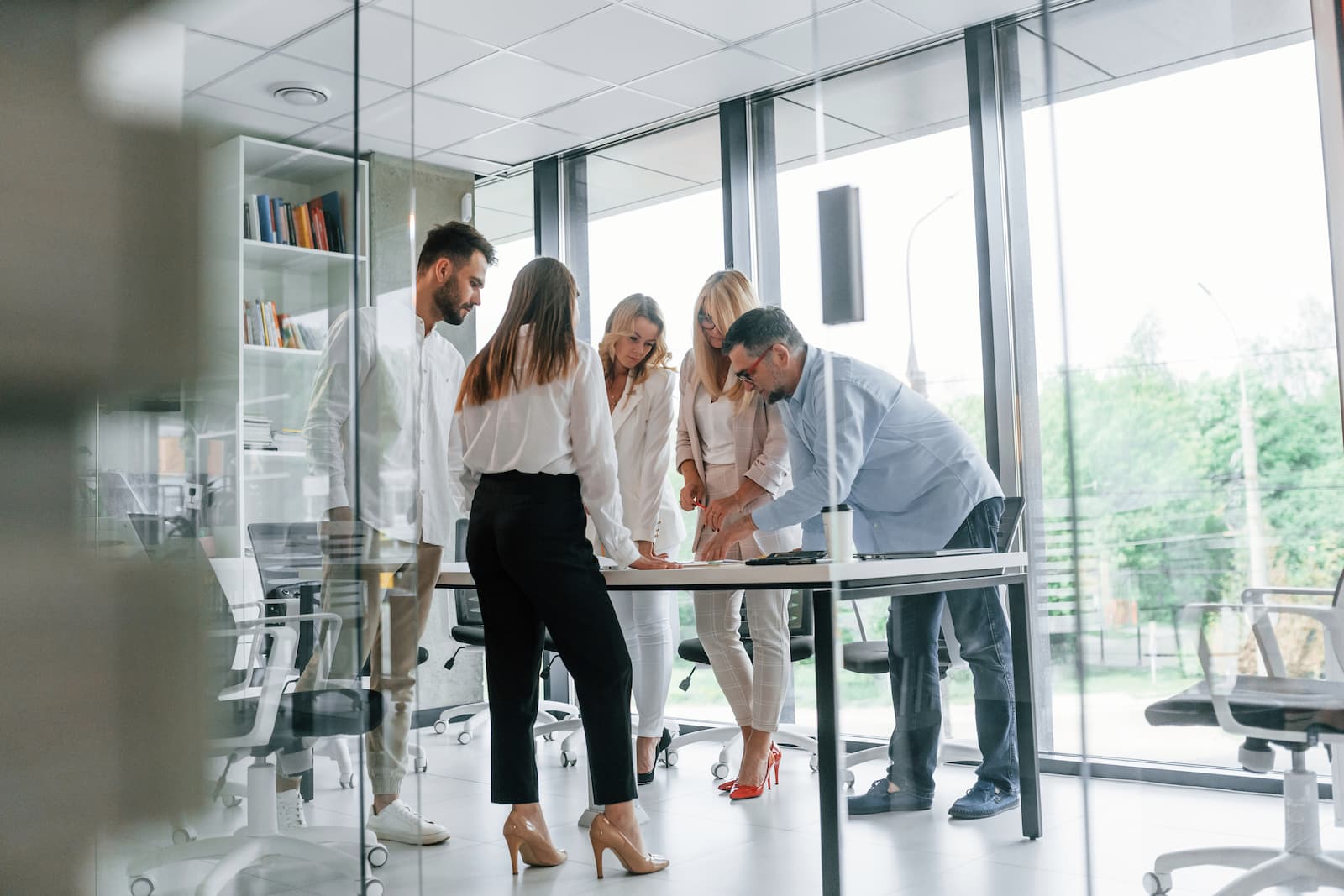 de pie junto a la mesa y un ventanal un gupo de empresarios profesionales analiza datos
