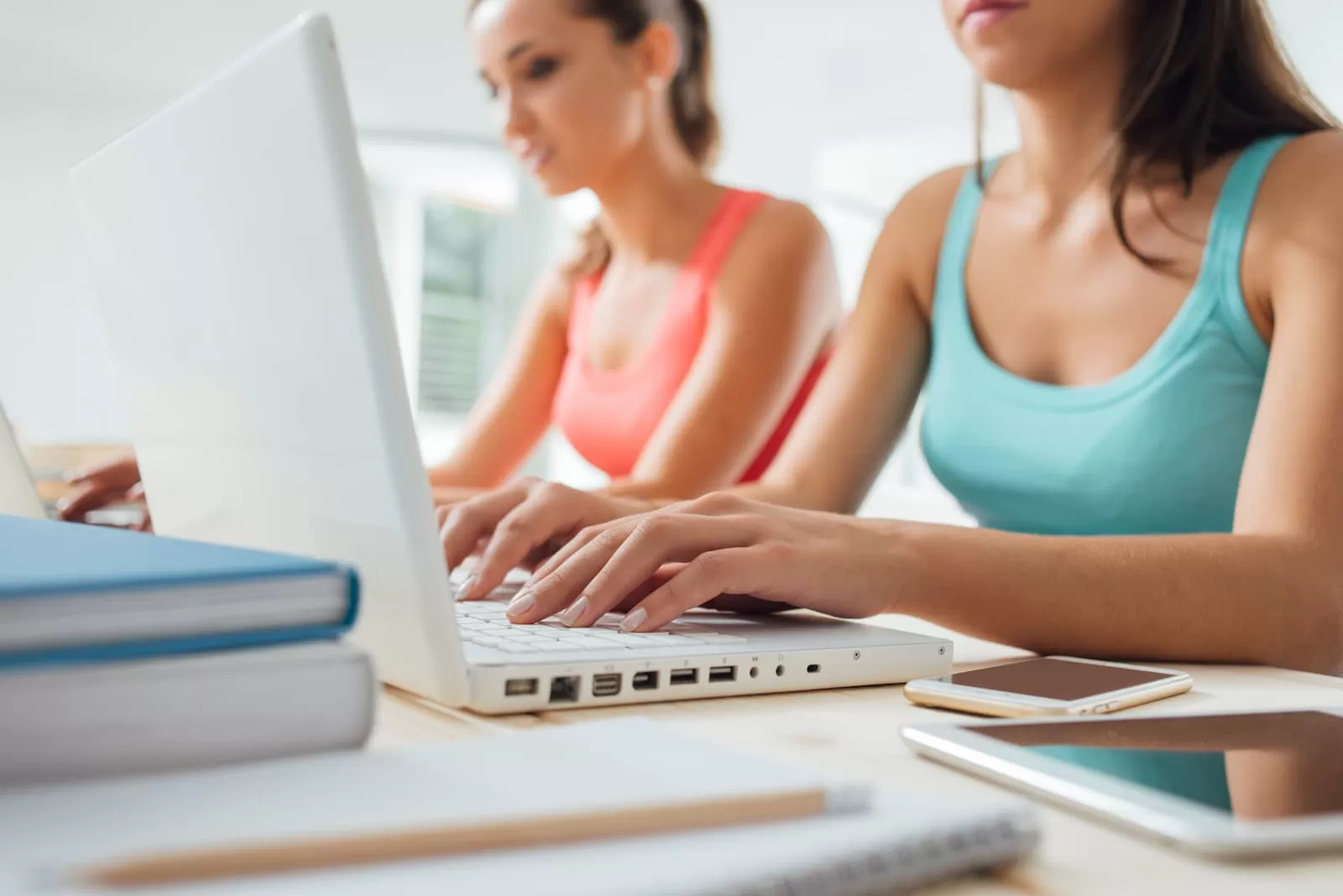 dos chicas jovenes teclean en el portatil mientras estudian