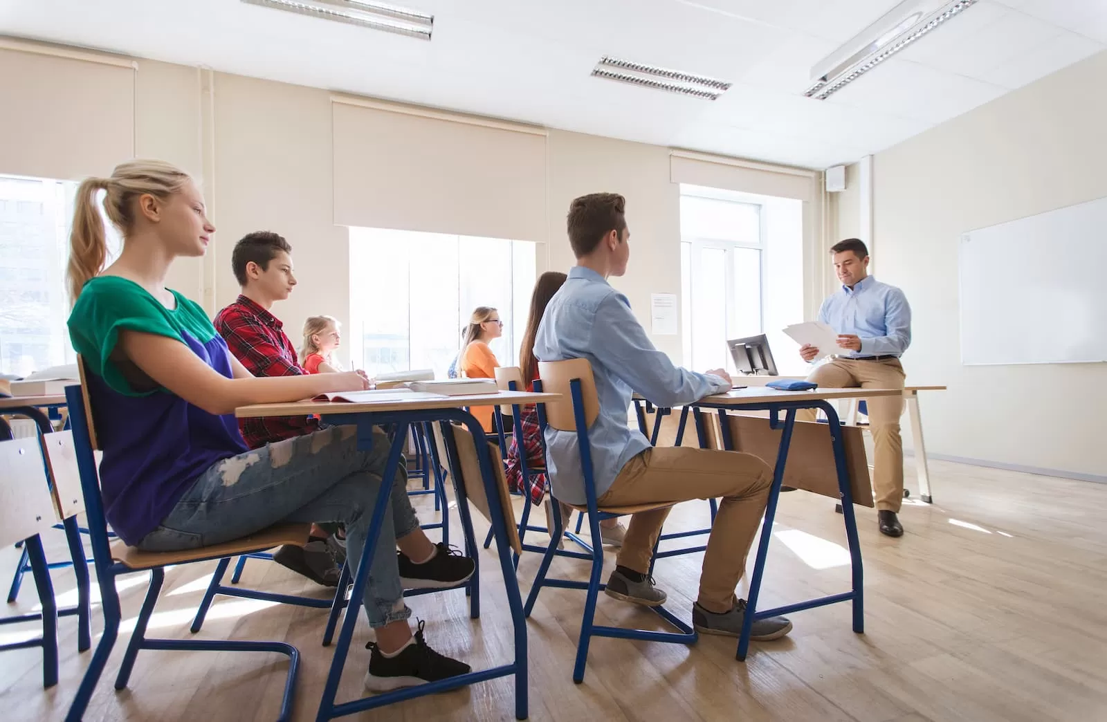 alumnos sentados en pupitres atienden a profesor