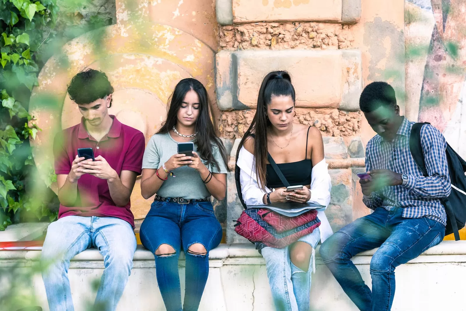 grupo de estudiantes multirraciales usando el móvil sentado al aire libre