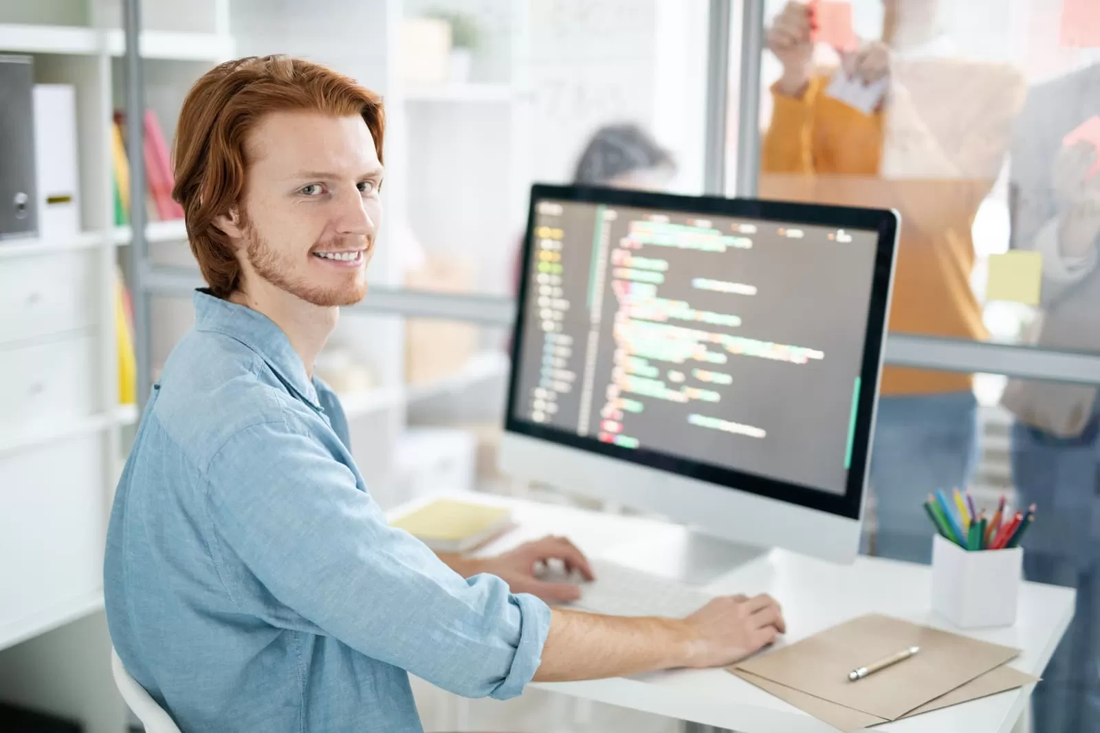 joven diseñador web sonrie sentado frente a su mac mientras programa