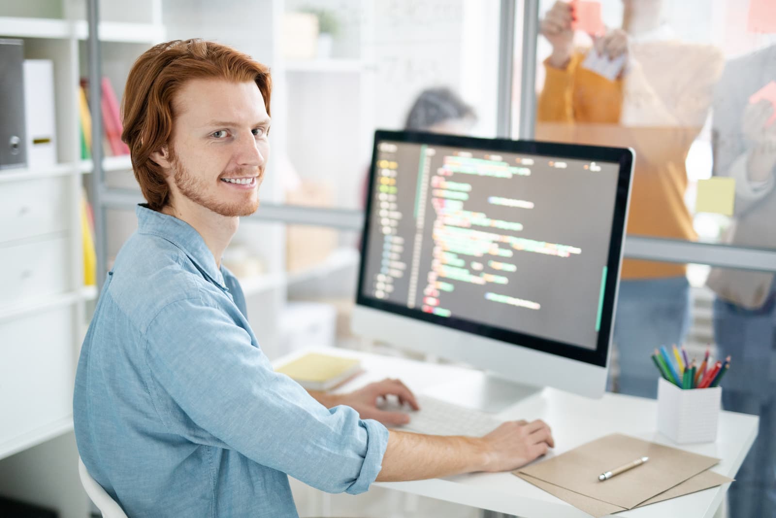joven diseñador web sonrie sentado frente a su mac mientras programa