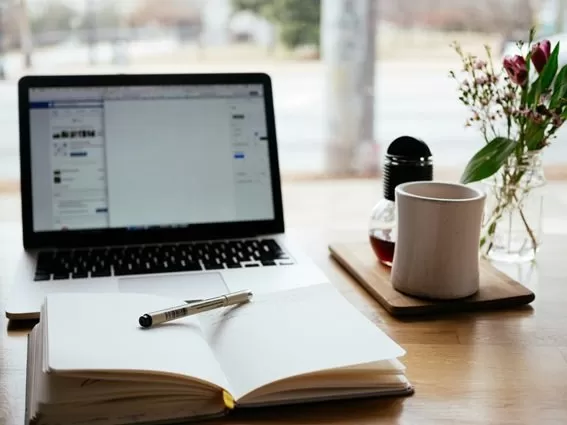 mesa con portatil cuaderno con apuntes y boli para estudiar online selectividad