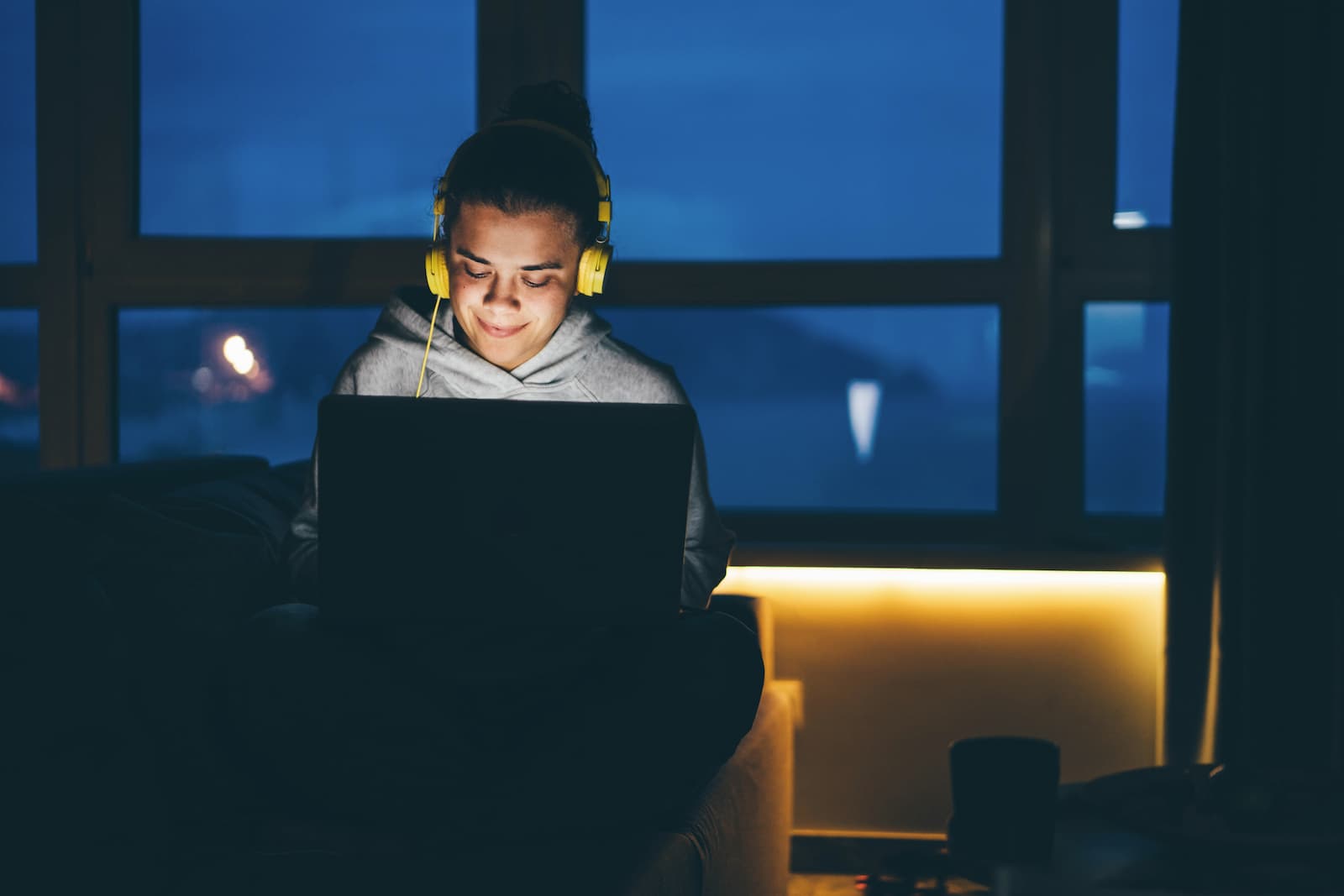 mujer estudia de noche con cascos amarillos frente al ordenador