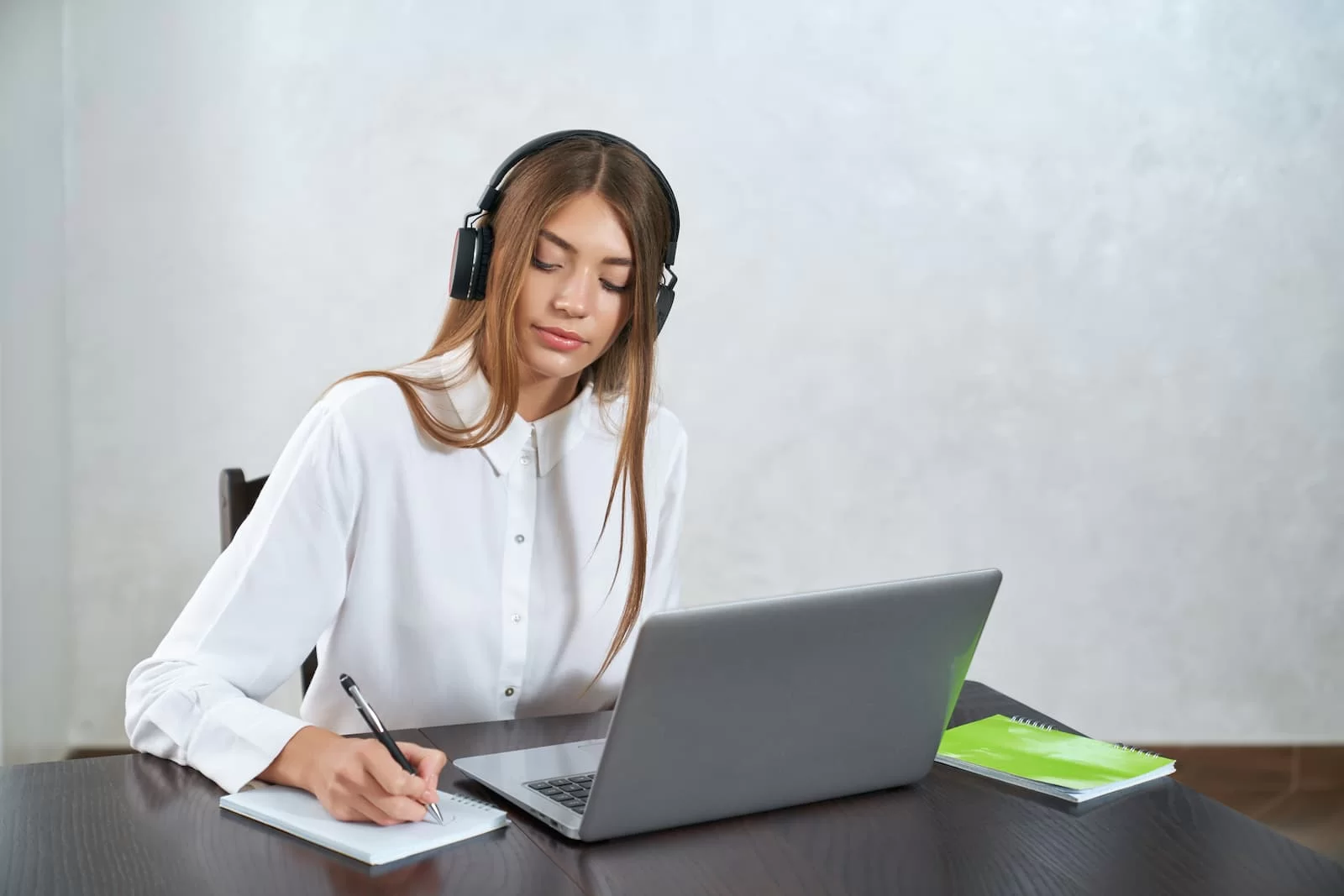 mujer joven rubia con camisa blanca sentada estudiando frente al portatil