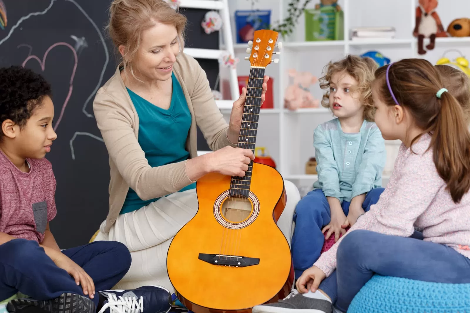 niños pequeños guarderia jardin de infantes sentados en una alfombra mientras la profesora toca la guitarra