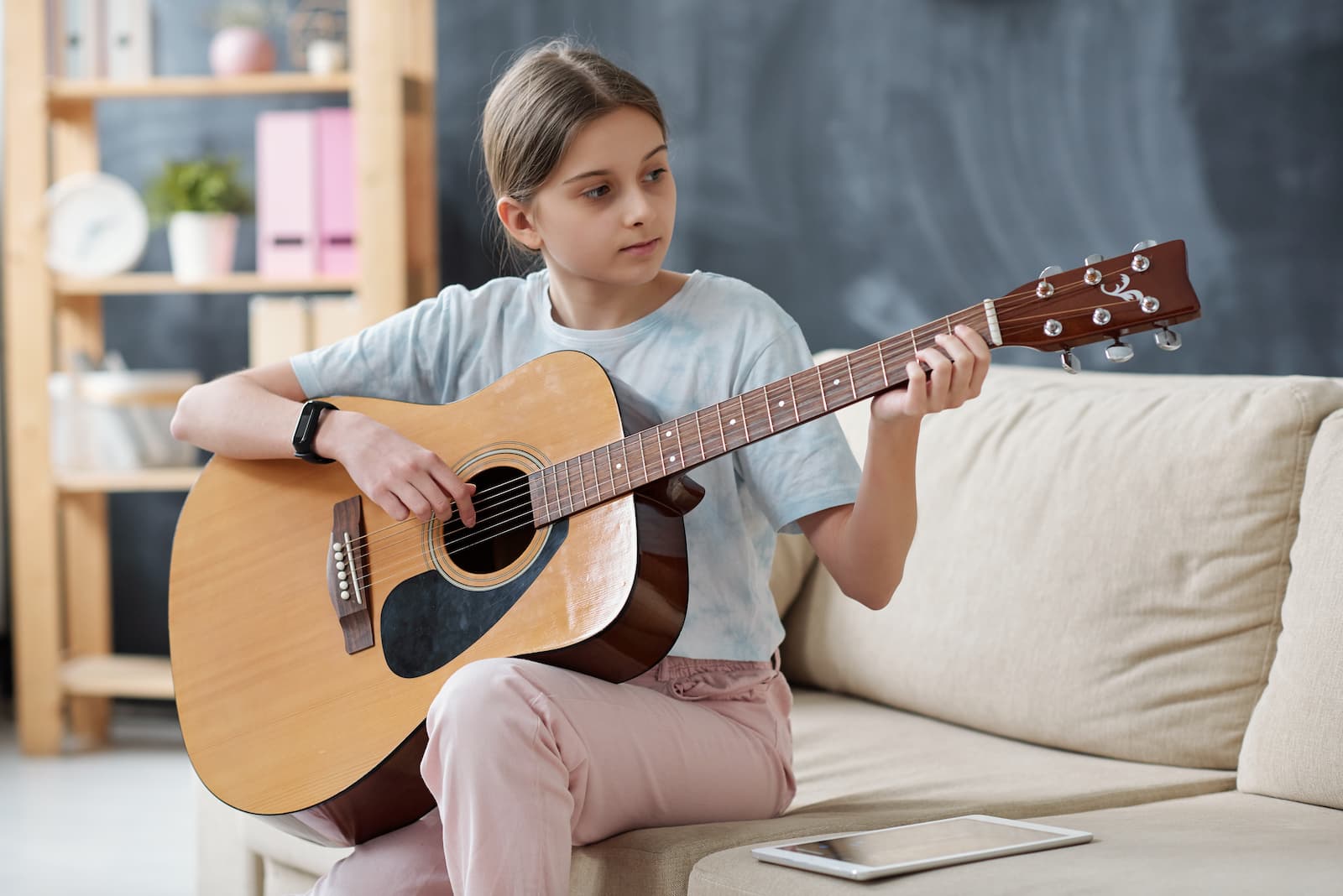 niña aprende a tocar la guitarra en el sofa junto a tablet