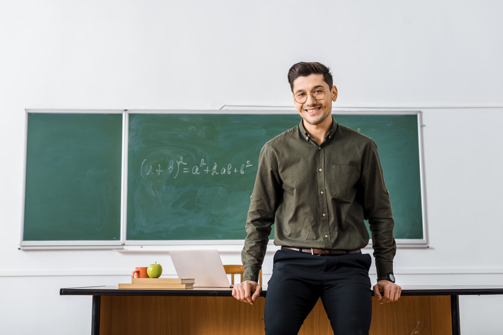 profesor joven sonriendo sentado en la mesa del profesor