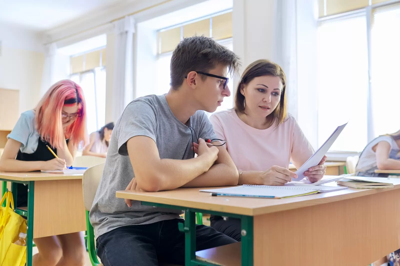 profesora de mediana edad sentada junto a estudiante adolescente enseña castellano