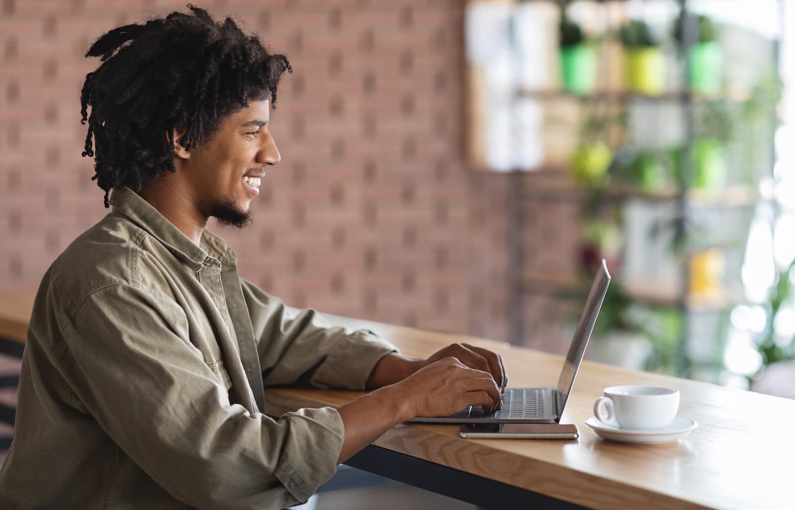trabajo remoto joven autonomo afroamericano que trabaja con un ordenador portatil en un cafe