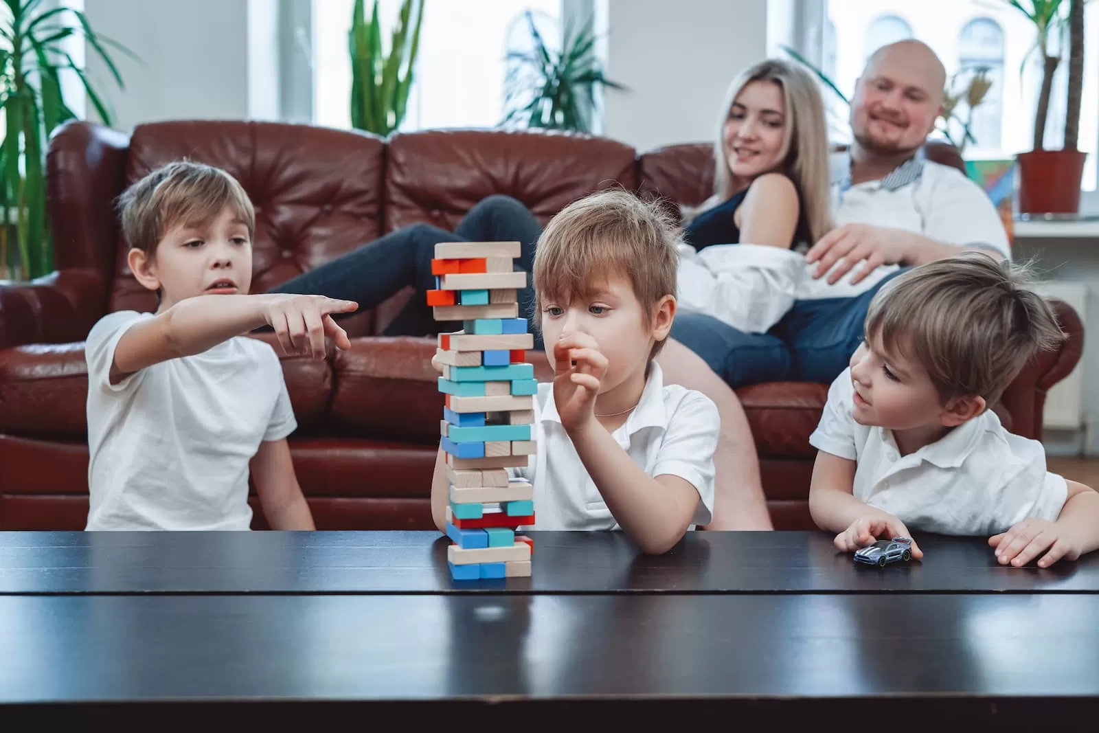 tres hermanos pequeños juegan sobre una mesa ante la mirada atenta de sus padres