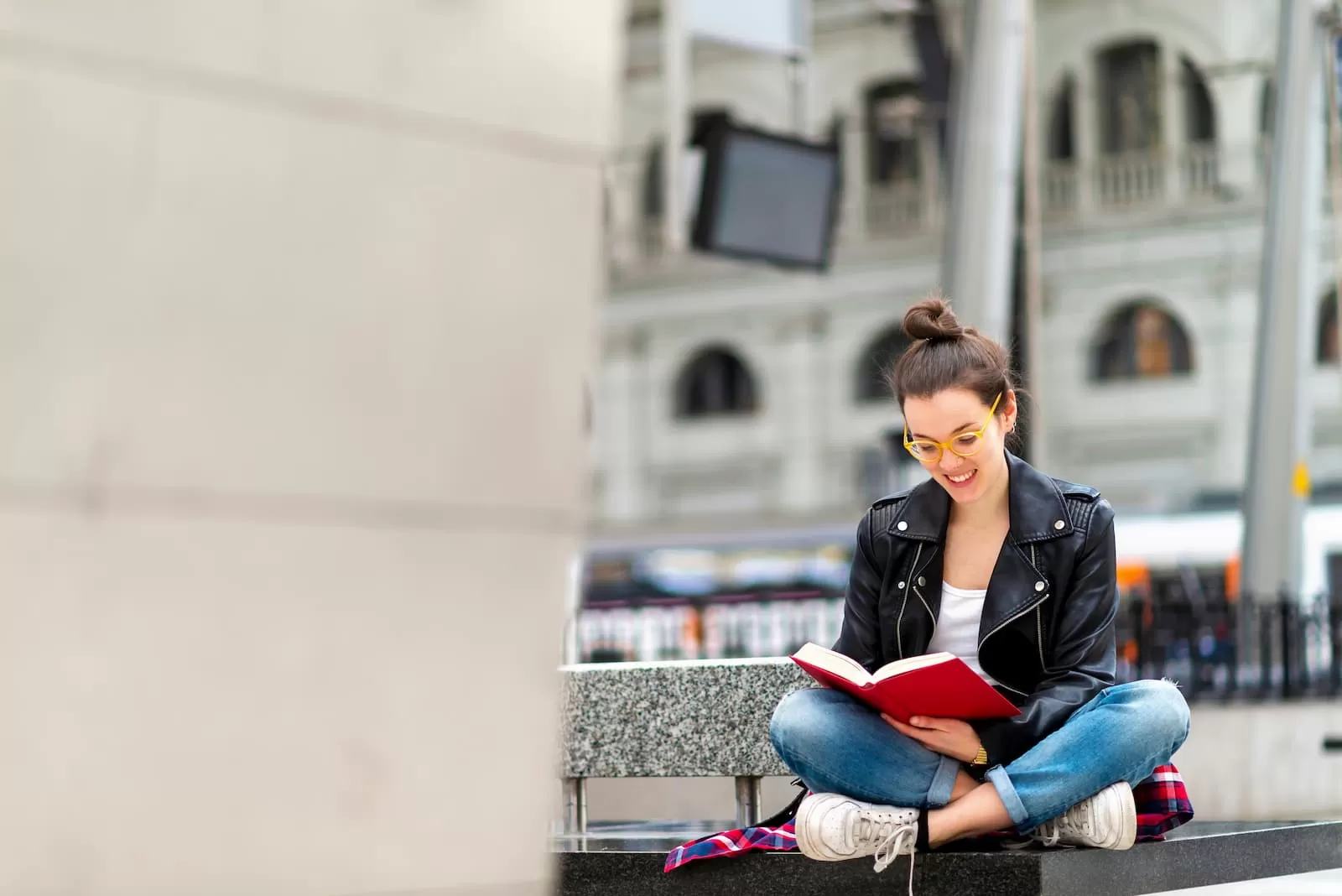 chica joven con gafas lee libro sentada en un banco