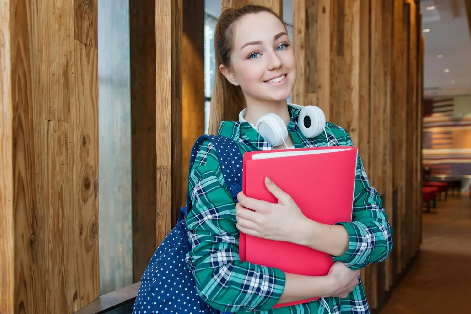 chica joven con cascos sujeta una carpeta roja de pie con camise de cuadros